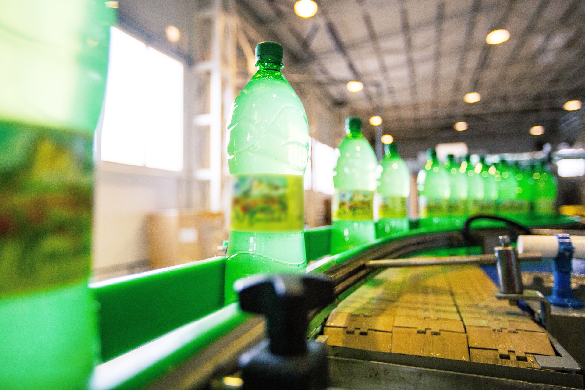 Bottles of green beverage moving along a production conveyor in a manufacturing facility